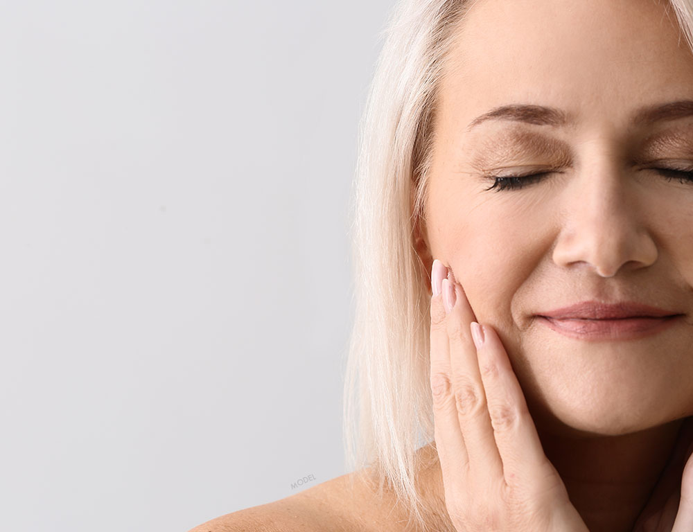 Close up headshot of a middle aged woman rubbing her cheeks