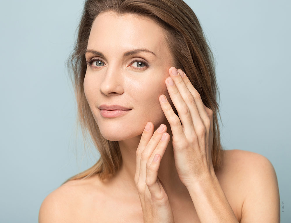 Woman with bare shoulders examining her cheeks