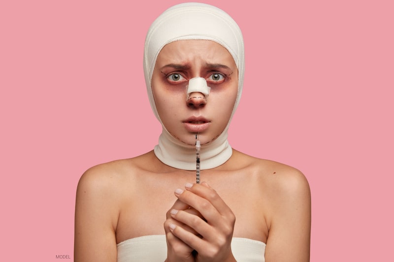  Woman in bandages after nose surgery and looking concerned while holding a syringe