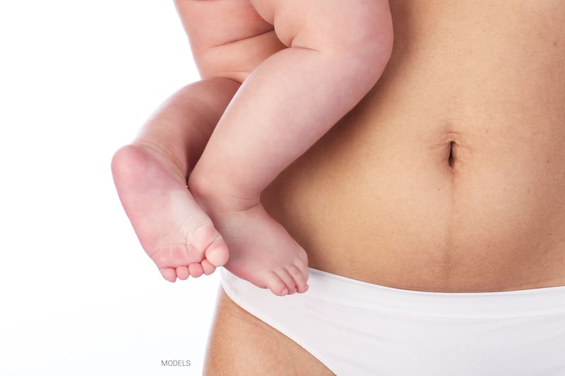 Close up of woman's abdomen holding a baby.